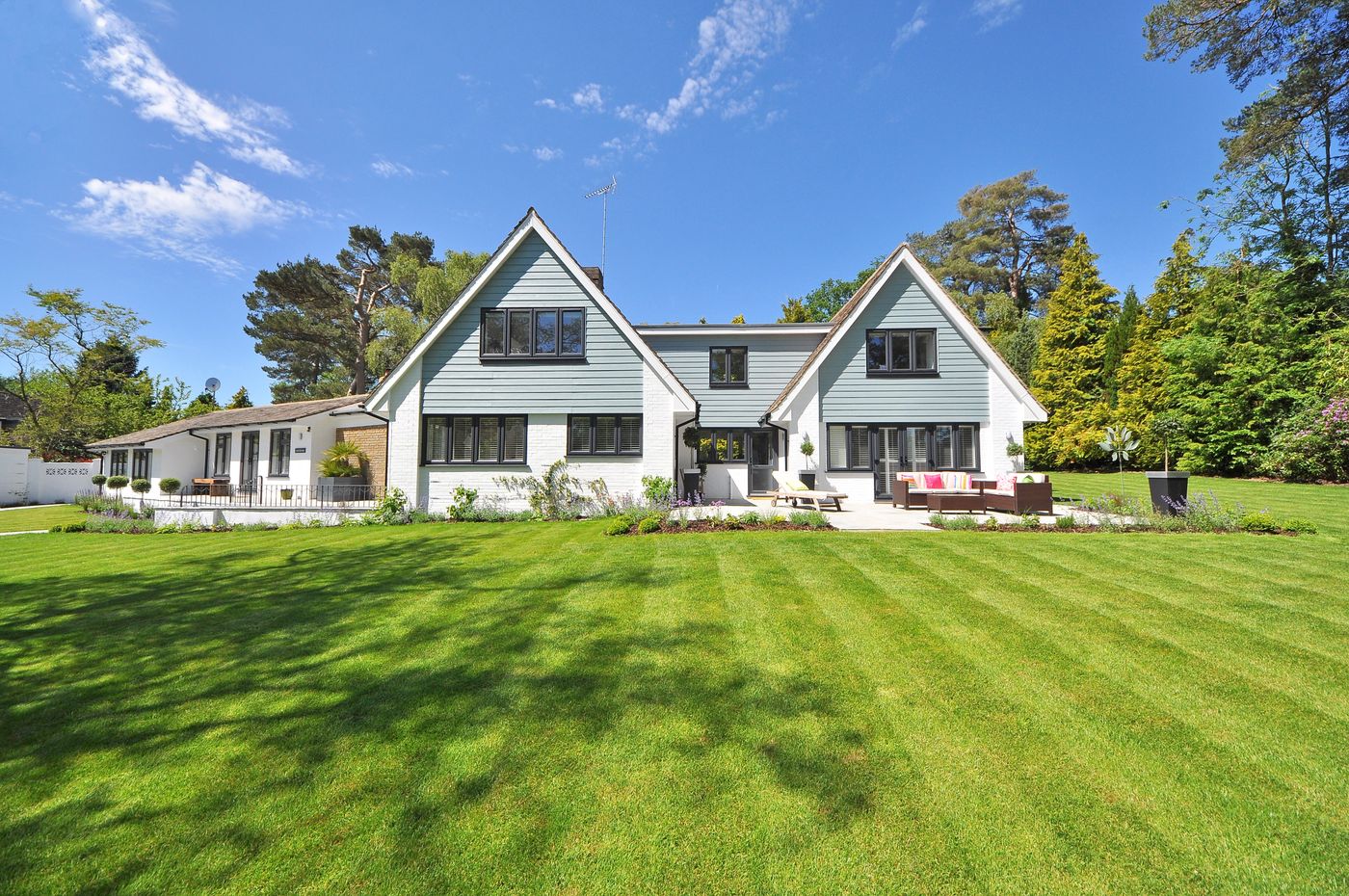 Wide freshly mown lawn cut into straight stripes running up to a white family home and planted garden beds